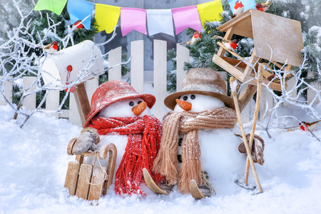 Two snowmen with skis and sledges against the background of a winter landscape on a sunny dayの写真素材