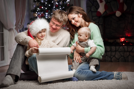 Parents with children are reading wish list for Santa Claus sitting on the floor near the Christmas tree and fireplaceの写真素材