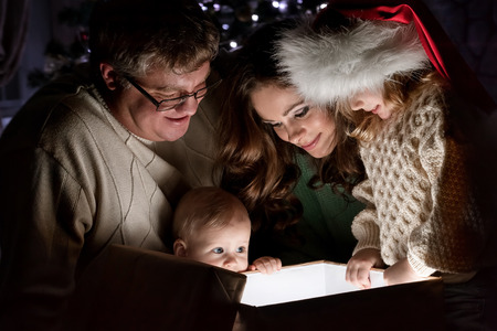 Parents with children is considered a magical gift on Christmas Eve under the Christmas tree by the fireplaceの写真素材