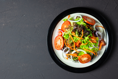 homemade vegetable salad tomato, carrot, onion, spinach, and lettuce on black board. top viewの写真素材
