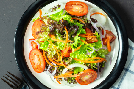 homemade vegetable salad tomato, carrot, onion, spinach, and lettuce on black board. top viewの写真素材