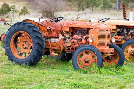 A derelict tractor, with parts missing and wires hanging out, parked in a fieldの写真素材
