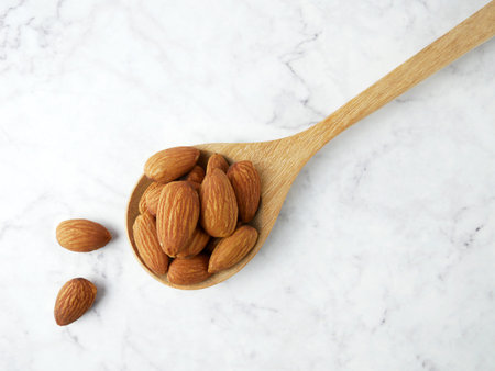 Almonds in wooden spoon on marble texture background.