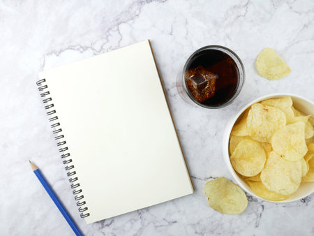 Soft drink and potato chips and book on marble background.