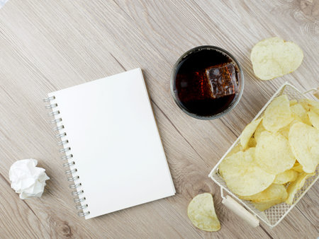 Soft drink and potato chips and book on wooden background.