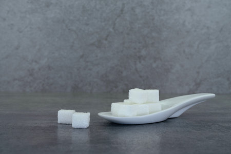 Sugar cubes in spoon on stone texture background.の写真素材