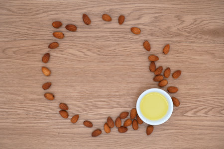 Almond oil in bowl and group of almond nuts on wooden texture background. Almond oil with almond seeds. Top view.の写真素材