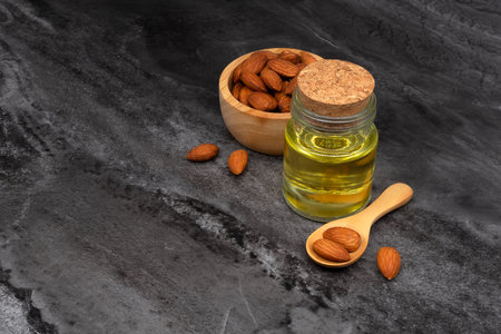 Almond oil in glass bottle and group of almond nuts on stone texture background. Almond oil with almond seeds.の写真素材