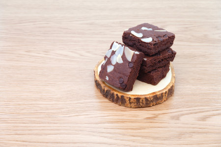 Brownies on wooden tray on wooden background. Chocolate brownie with sliced almond nuts toppings. Chocolate Brownie pieces. selective focus.の写真素材