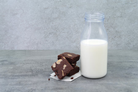 Brownies and milk bottle on stone texture background. Chocolate brownie with sliced almond nuts toppings. Chocolate Brownie pieces. selective focus.の写真素材