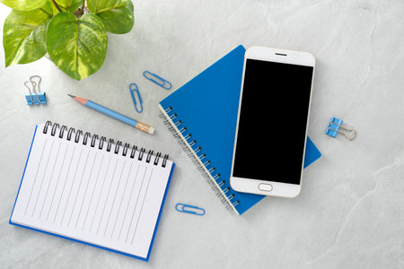 Mobile phone with blank mockup screen and book on stone texture background.Work desk. Top view. Flat lay.の写真素材