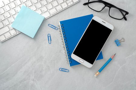 Mobile phone with blank mockup screen and book on stone texture background.Work desk. Top view. Flat lay.の写真素材