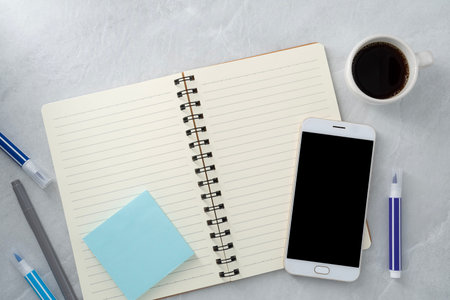 Mobile phone with blank mockup screen and book and coffee on stone texture background.Work desk. Top...