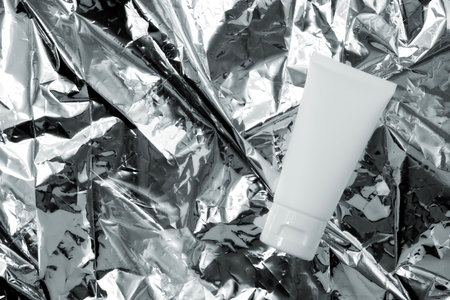 White cream tube on silver paper texture background. For mockup.