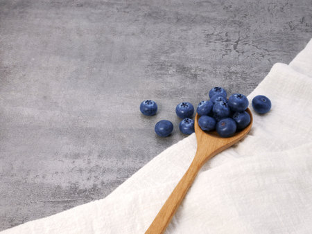 Blueberries in wooden spoon with cloth on stone texture backgroundの写真素材