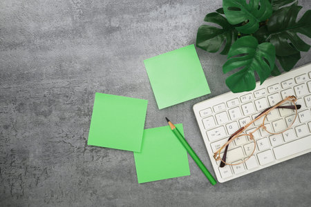 Top view of workplace with keyboard and green stationery on stone texture background