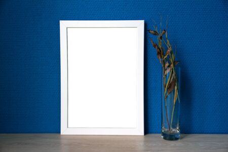 White frame and glass vase with branches with blue wallpaperの写真素材