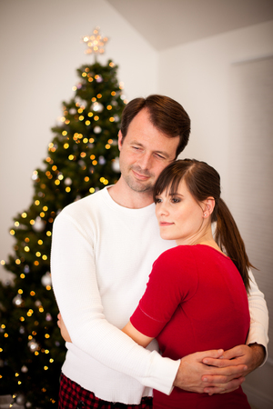 Young Couple Hugging by Christmas Tree at Homeの写真素材