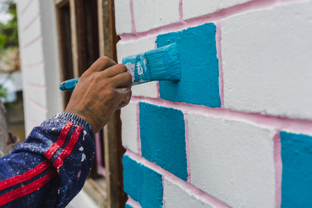 Painter's hand holding a brush while painting on a wall with blue color.の写真素材