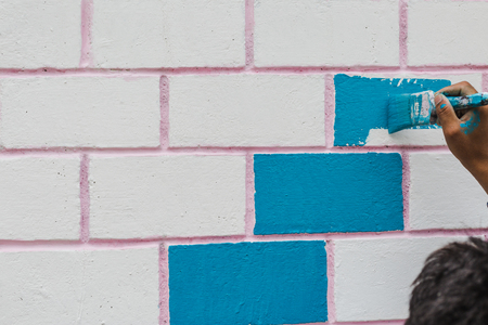 Painter's hand holding a brush while painting on a wall with blue color.の写真素材