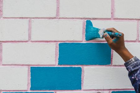 Painter's hand holding a brush while painting on a wall with blue color.の写真素材
