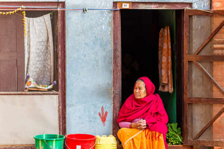 Kathmandu, Nepal - November 24, 2018 : Old Nepalese woman looking outside while sitting on the door at house in Kathmandu. Casual Lifestyle of older people.のeditorial素材