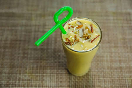 Homemade Fresh Mango Lassi with Nuts and Straw on the table. Sweet Mango Lassi,Cold Summer drinkの写真素材