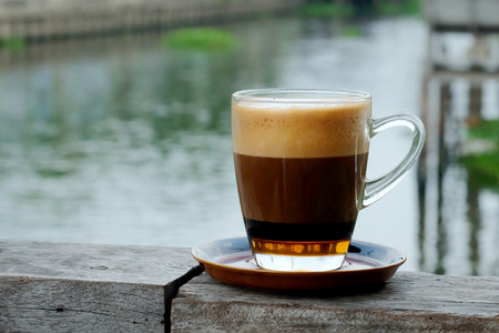Special recipe hot coffee with milk on top and syrup in clear coffee cup served in a shop beside the river in a relax time with space for write wording, good environment for meet friend or loversの写真素材