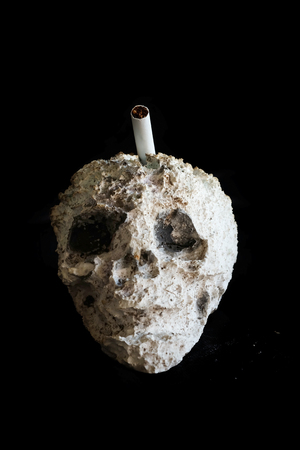 Skull shape cigarette ash tray and space for write wording, a warning symbolic to alert cigarette consumer realize danger of smoking that affect health and finance problem to themselves and familyの写真素材