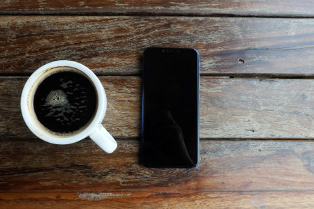 Flat lay photo of smartphone and black coffee on wood table with space for write wording, innovation...