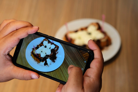 Taking coffee and bread with banana photo by smartphone camera, trendy lifestyle new generation to take and share to social network, opportunity of well decorate coffee and new technology smartphoneの写真素材