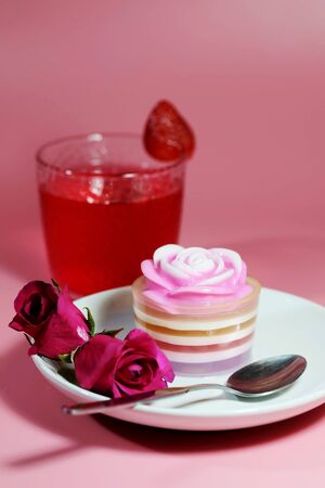 Multilayer sweet coconut fruit jelly with beverage, strawberry and red roses on white plate and pink background and space for write wording for happiness moment. Unhealthy dessert high sugar and fat.の写真素材