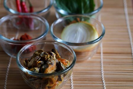 Set of important ingredients for making Stir Fried Mussels with Thai Basil and Chili on wood mat and space for write wording containing Mussels, Onion, Red Chili Paste, Chili and Thai Basil leavesの写真素材