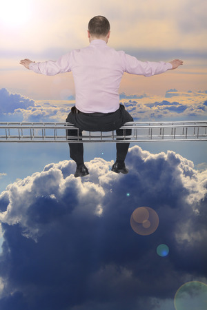 Businessman sitting on light metal girder beam with cloud sky in backgroundの写真素材