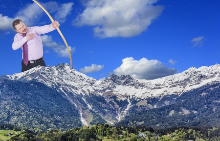 Businessman practicing archery and mountain valley in foregroundの写真素材