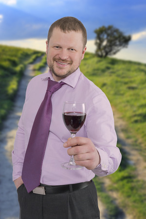 Businessman holding glass of wine with sunset landscape in backgroundの写真素材