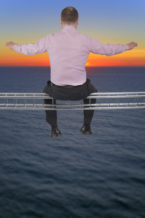 Businessman sitting on light metal girder beam looking at sunsetの写真素材