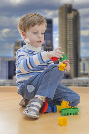 Boy playing with plastic construction with contemporary buildings in backgroundの写真素材