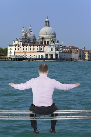 Businessman sitting on light metal girder beam with view of Venice, Italy in backgroundの写真素材