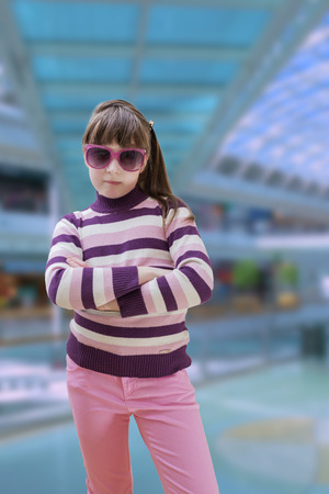 Teenage girl in pink wears sunglasses with modern shopping mall in backgroundの写真素材