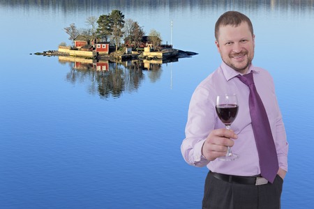 Businessman holding glass of wine with sea island in backgroundの写真素材