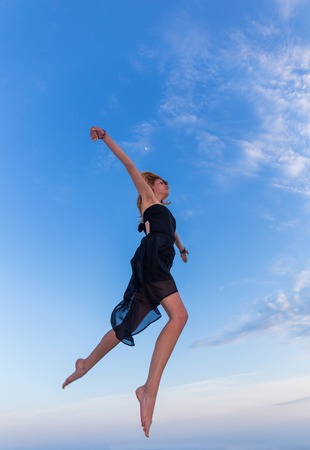 Young beautiful woman jumping on blue sky backgroundの写真素材