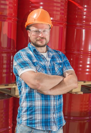 Worker in safety helmet standig in front of metal barrelsの写真素材