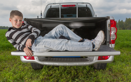 boy laying on car trunk on natural backgroundの写真素材