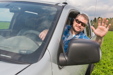 Man sitting in a car on driver's place and raising his hand in a greetingの写真素材