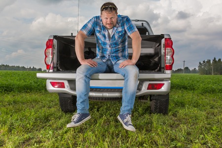 Solid man sitting on car trunk on natural backgroundの写真素材