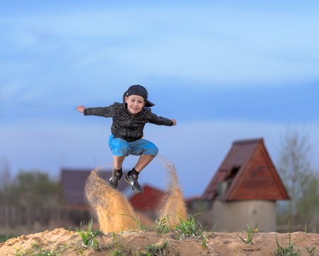 Boy jumping on the sand with countryside buildings on backgroundの写真素材