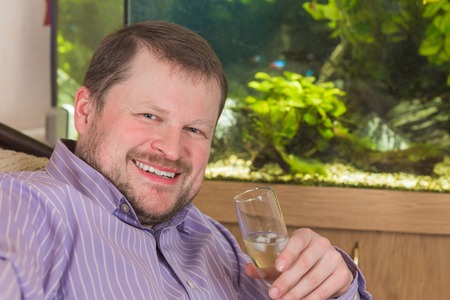 Man sitting in armchair with glass of champaign with aquarium on backgroundの写真素材