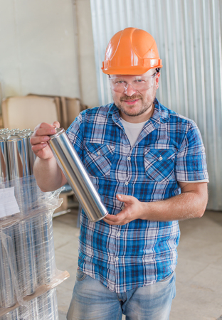 Worker smiling in safety helmet at the storage with tin blank tubesの写真素材