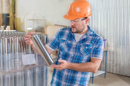 Worker smiling in safety helmet at the storage with tin blank tubesの写真素材